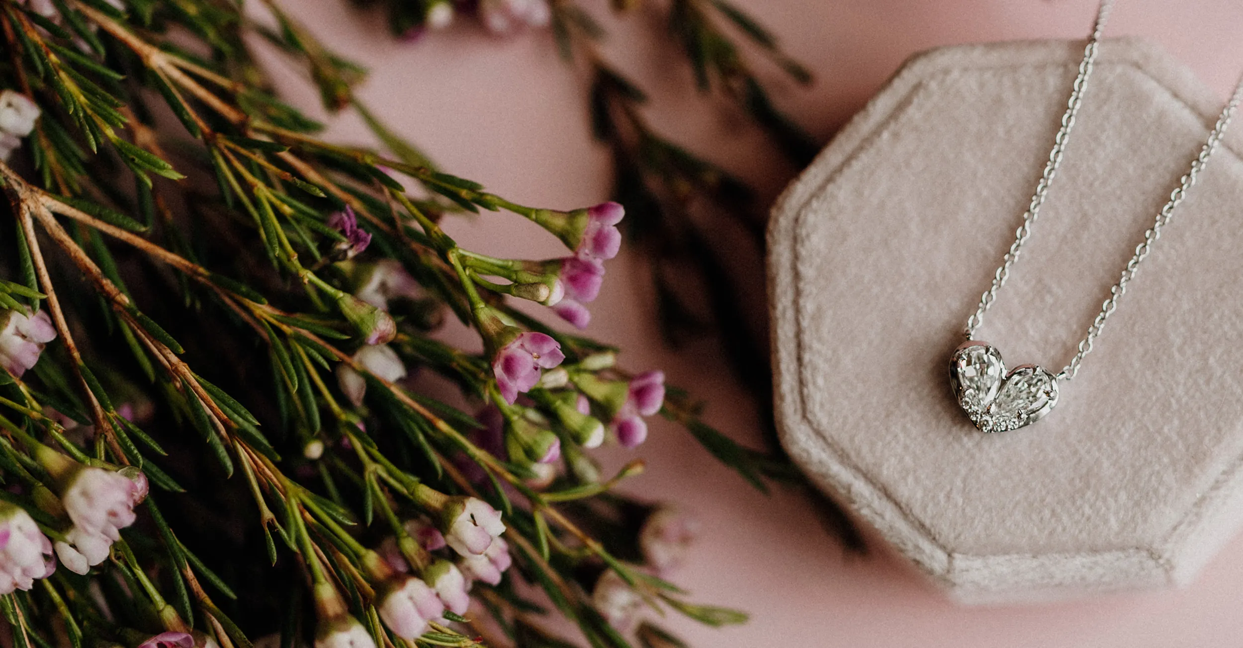 Heart-shaped diamond necklace on a soft display with flowers, promoting Koerbers Fine Jewelry. Click to read more testimonials.