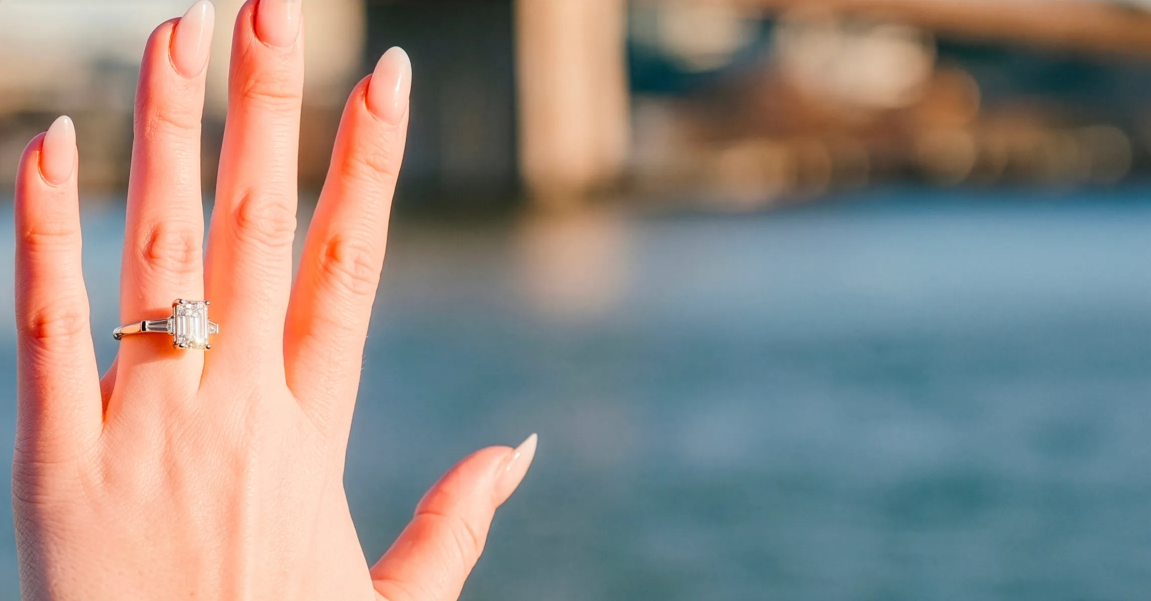 A hand with a diamond ring is held up against a blurred outdoor background. Schedule Consultation.