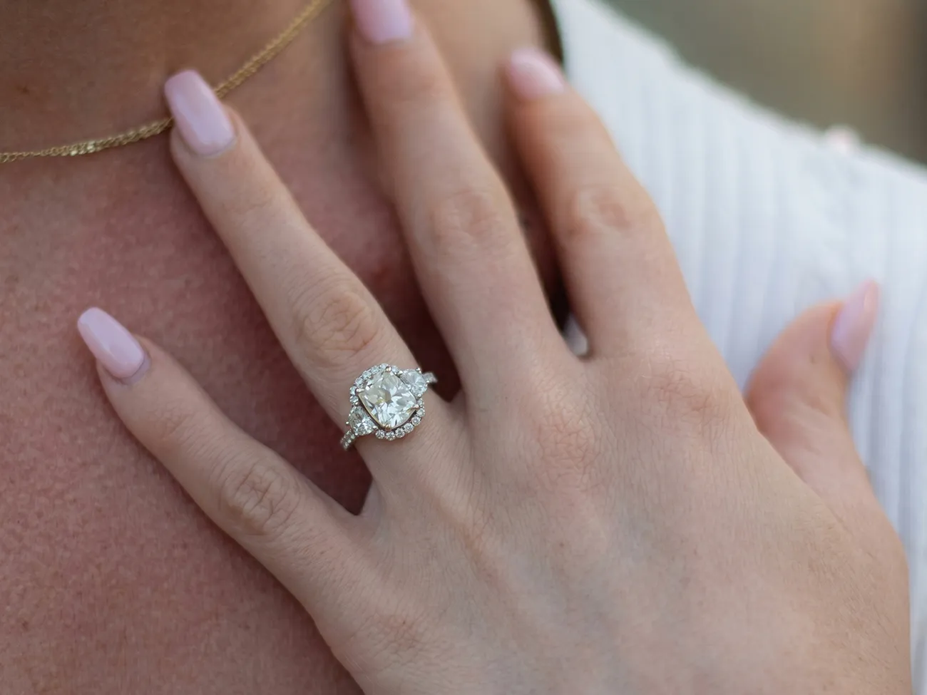 A hand with a diamond engagement ring and pink nails rests on the chest.