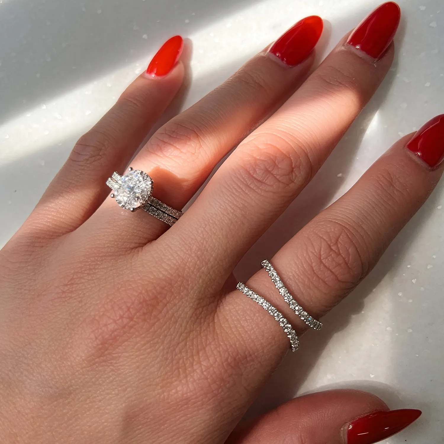 A hand with red nails wearing diamond rings, including an engagement ring.