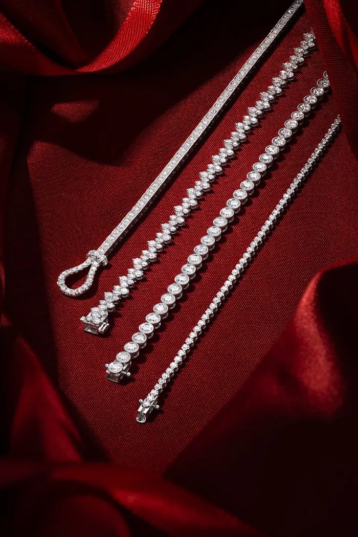 Elegant diamond tennis bracelets on red satin background.