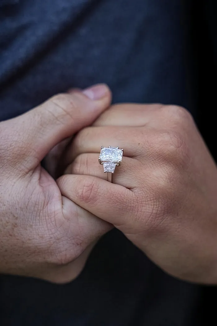 Hands holding with a large diamond engagement ring prominently displayed.