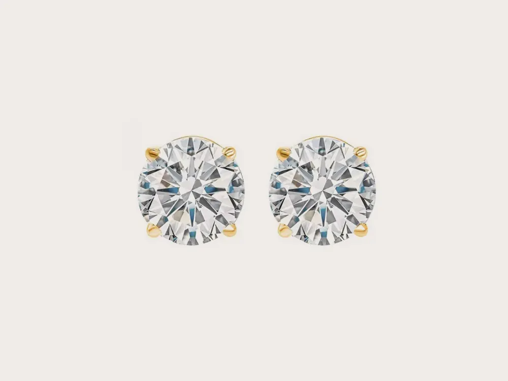 Diamond stud earrings with gold prongs on a white background. Click to shop earrings.