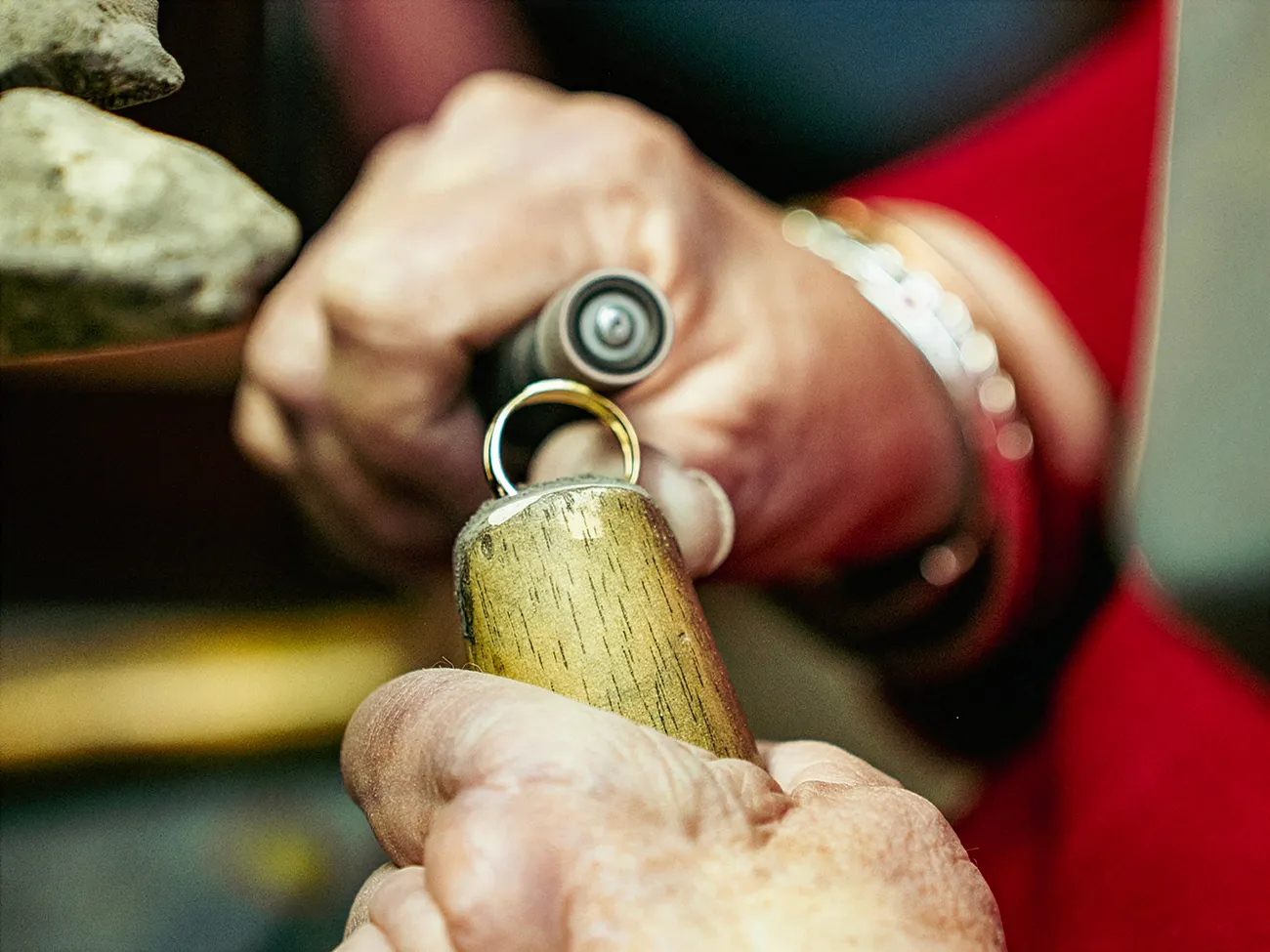 Hands working on jewelry repair with a tool and wooden holder.