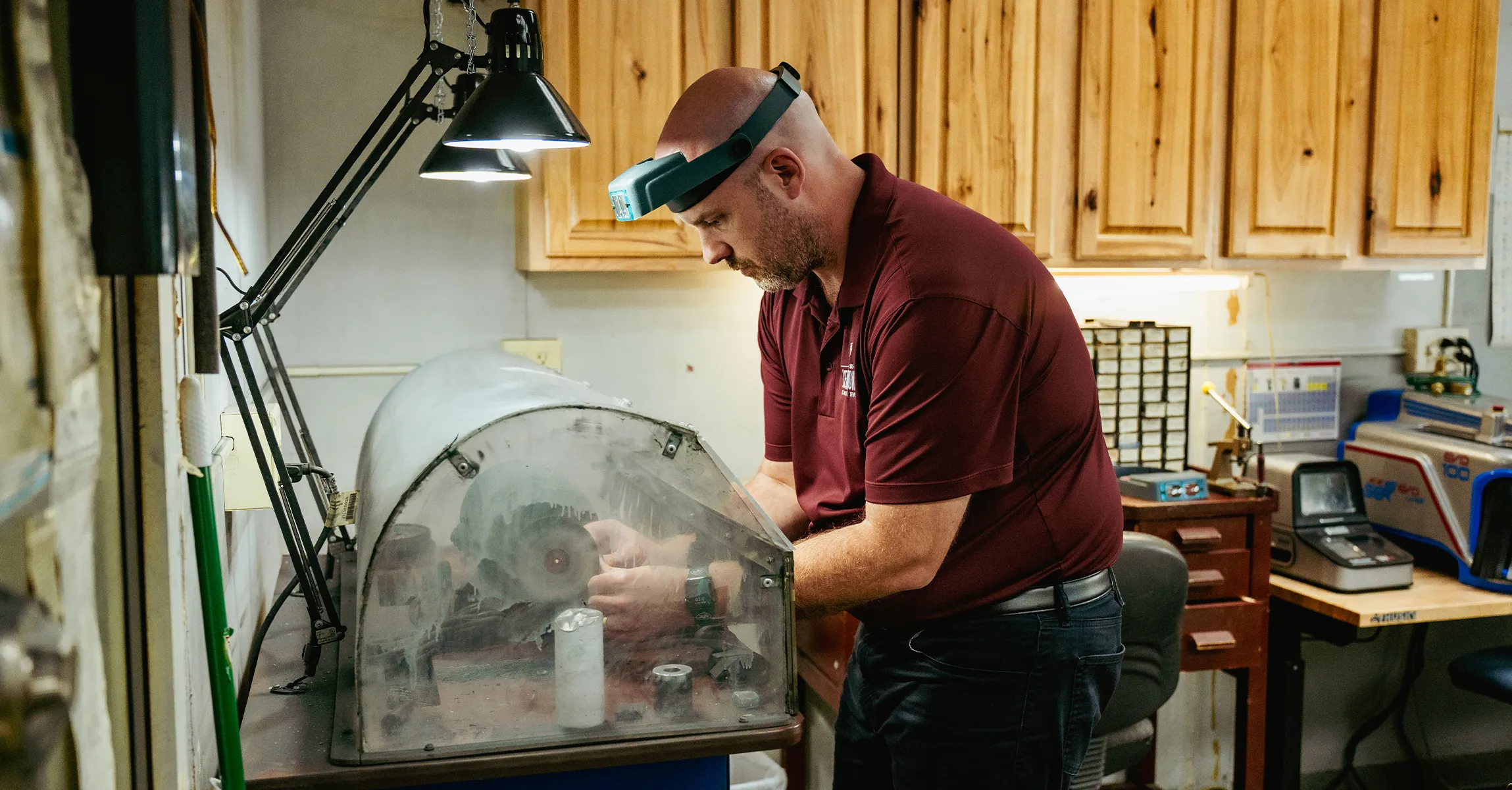 Man working on jewelry under a lamp in a workshop. Start a Project at Lennon's W.B. Wilcox Jewelers.