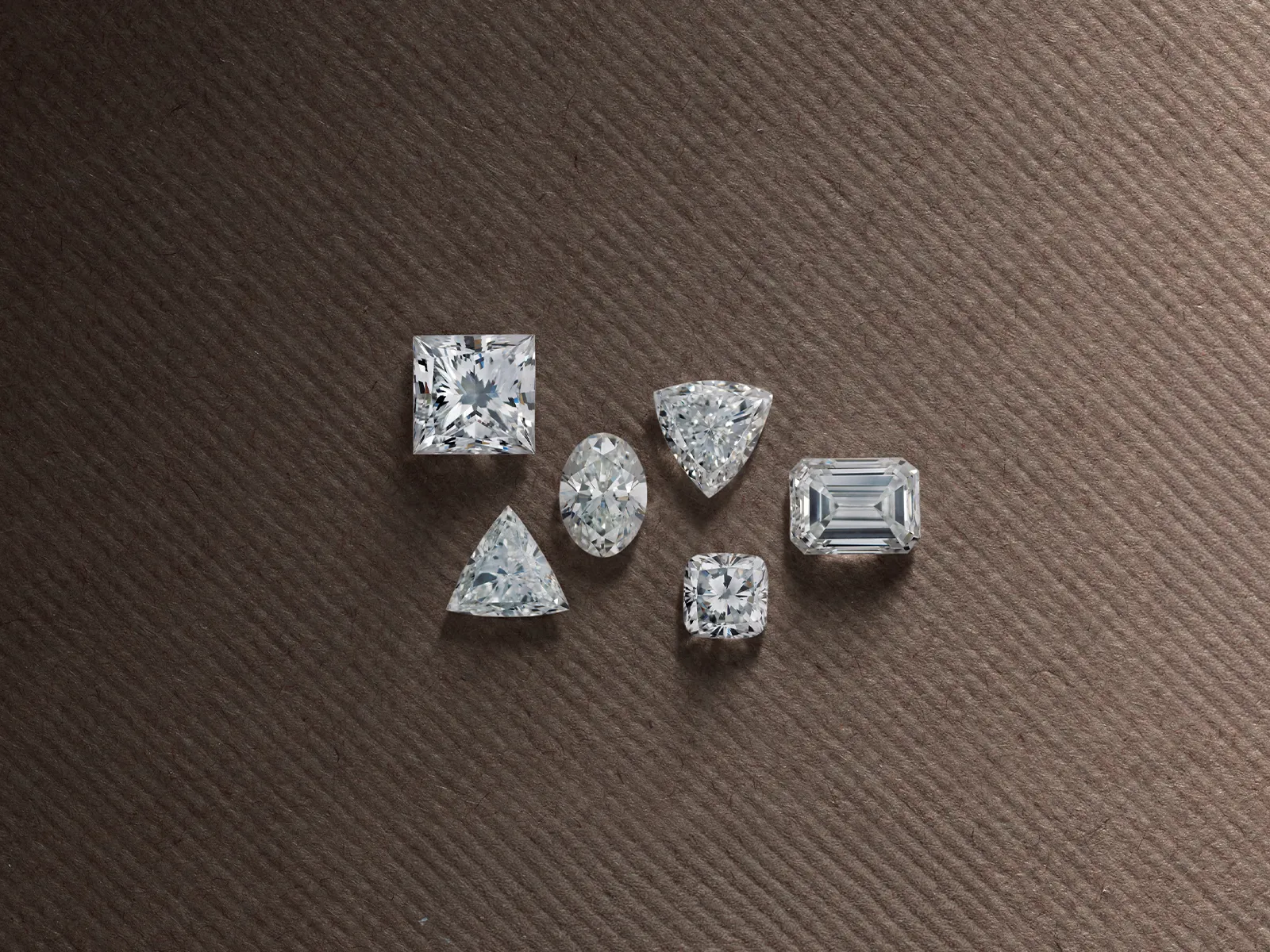 Loose diamonds in various cuts on a textured brown surface at Marshall's Jewelers, Bellingham MA.