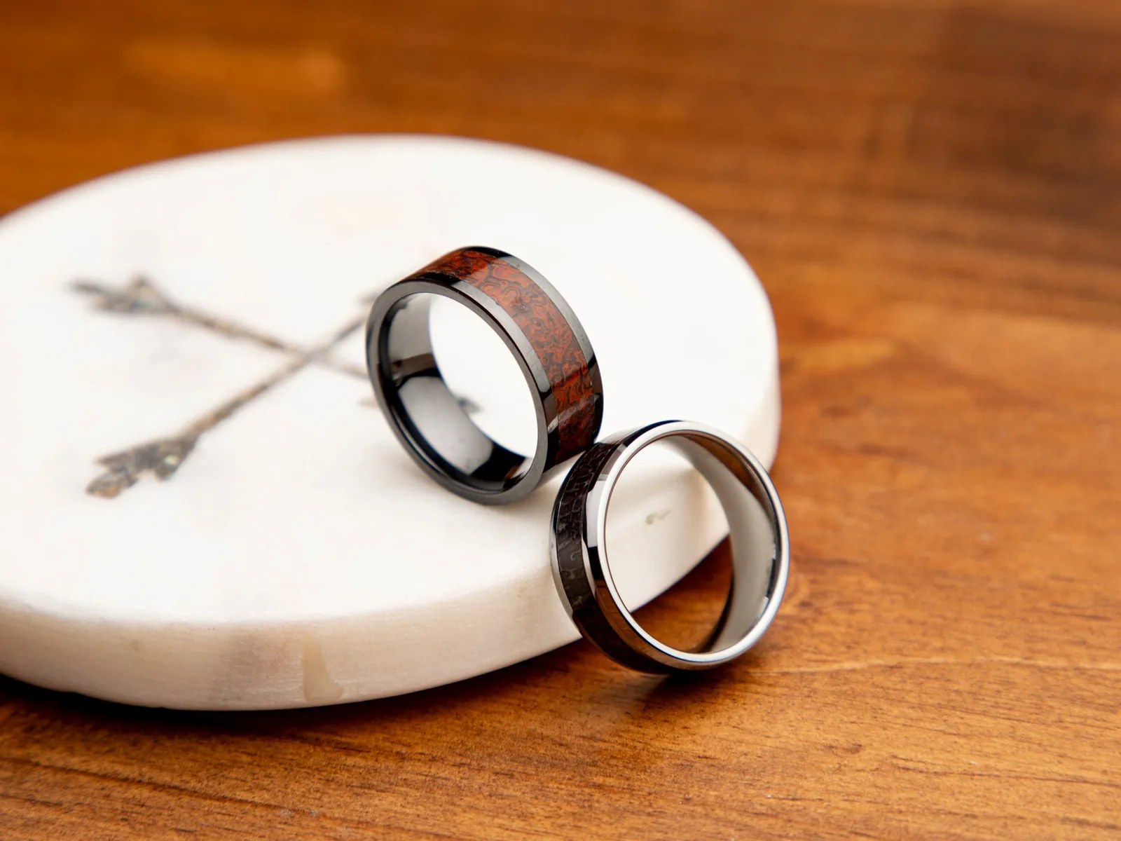 Men's wedding bands with rose gold and black accents on a textured surface.