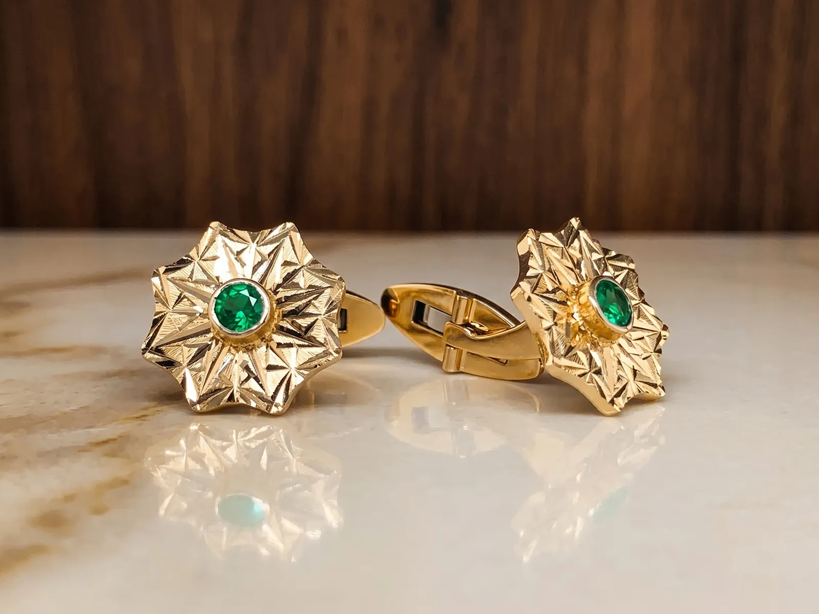 Gold cufflinks with star-shaped design and green gemstone center on a marble surface.