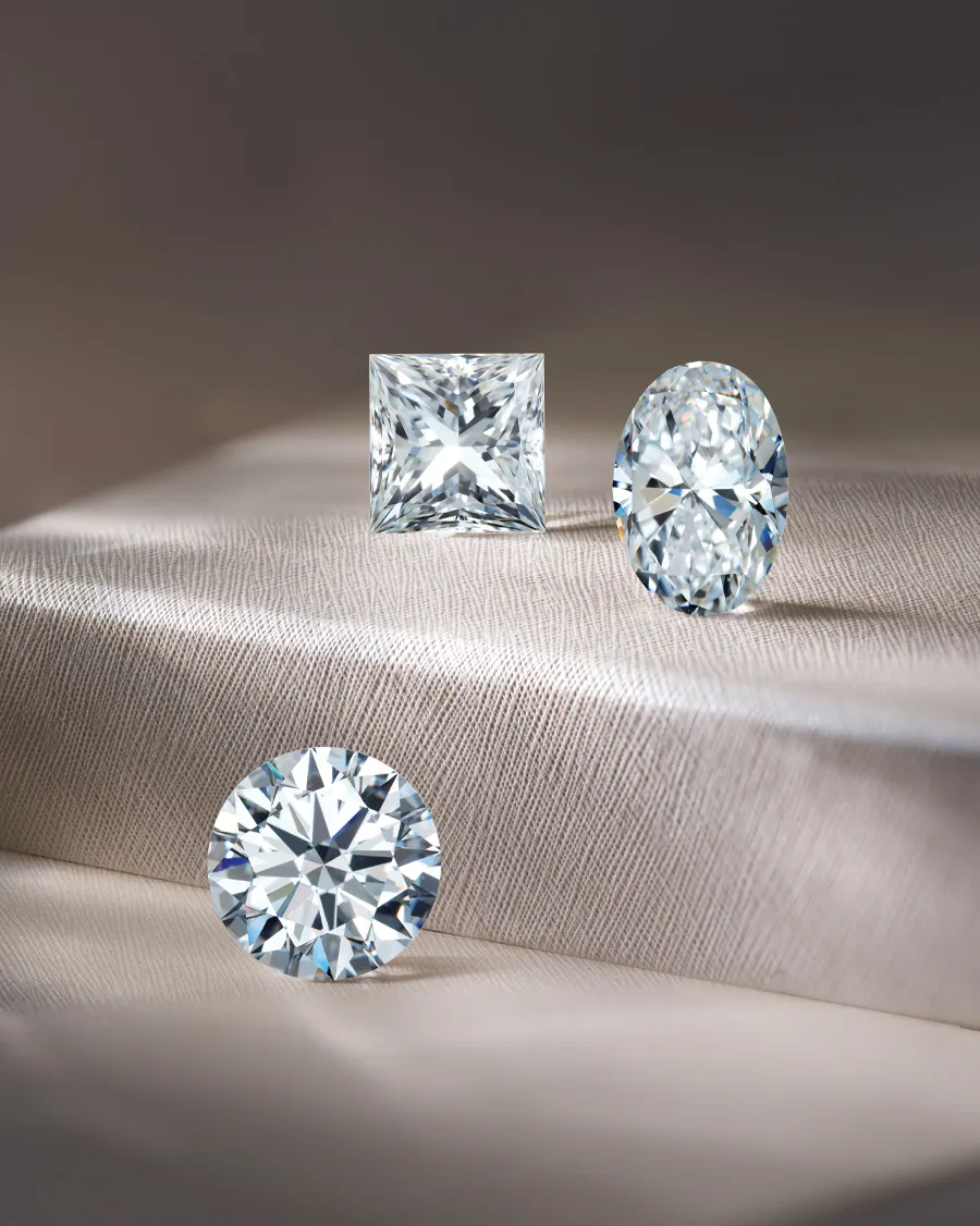 Three sparkling diamonds in different cuts on a soft fabric background.