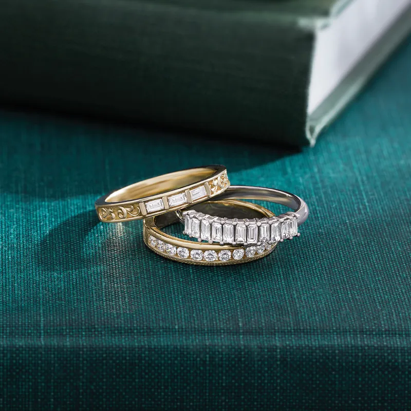 Three elegant anniversary bands featuring gold and silver designs with diamonds, displayed on a teal surface.