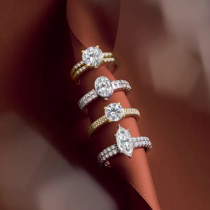 Four elegant engagement rings displayed on a brown fabric background.