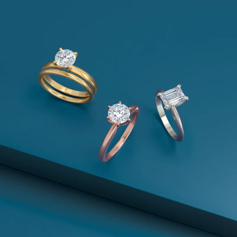 Three elegant engagement rings in gold, rose gold, and silver settings, featuring sparkling diamonds.