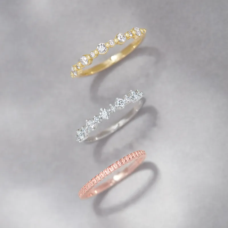Three elegant eternity bands in gold, silver, and rose gold, featuring sparkling diamonds, displayed on a gray background.