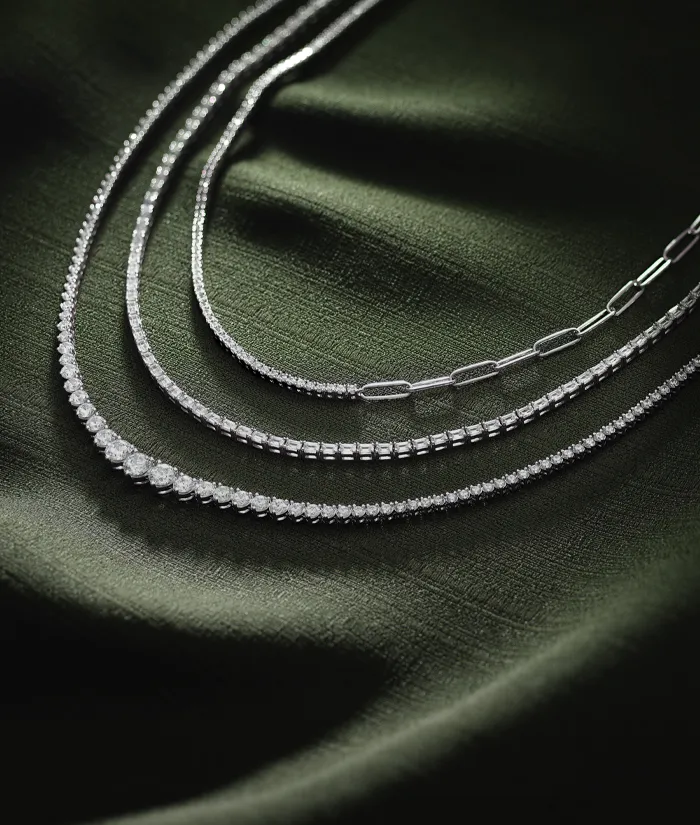 Three elegant silver necklaces displayed on a dark green fabric background.