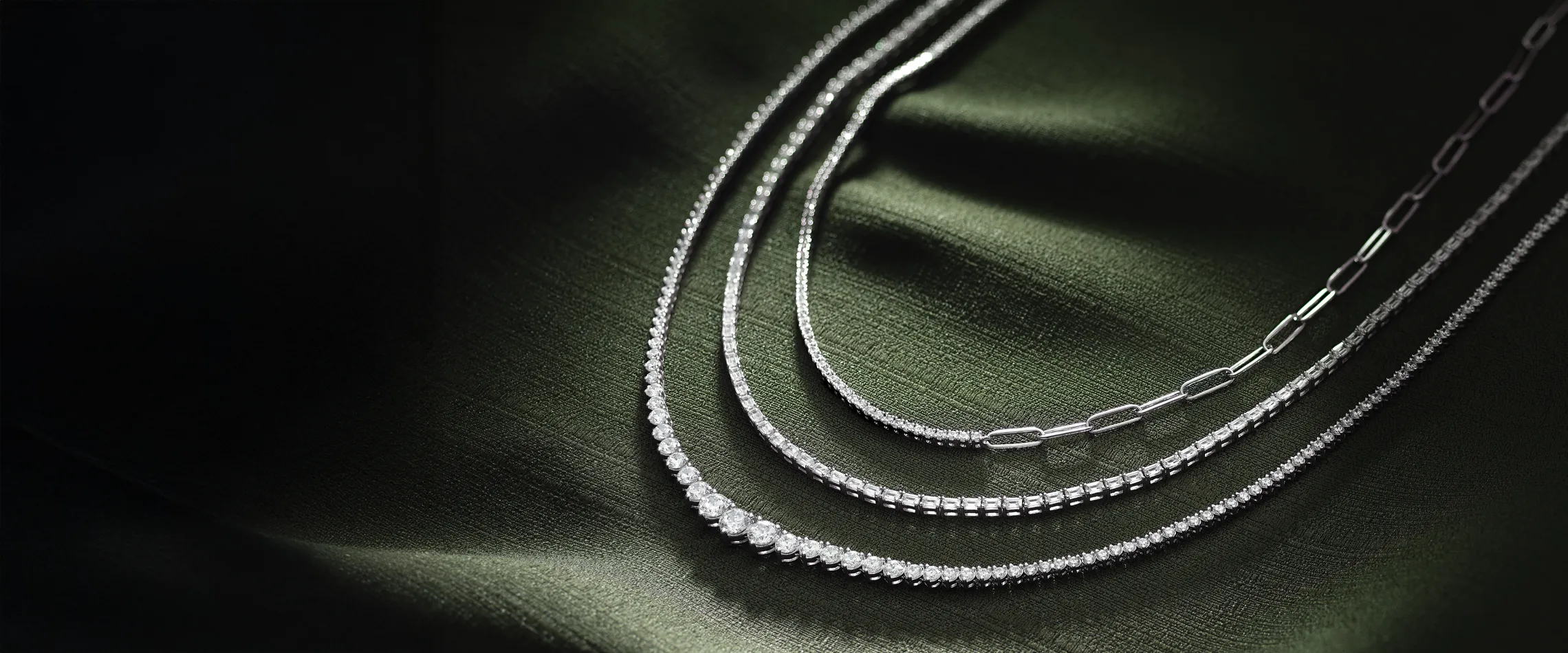 Three elegant silver necklaces displayed on a dark green fabric background.