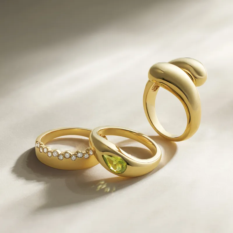 Three elegant gold rings featuring diamonds and a green gemstone, displayed on a soft surface.