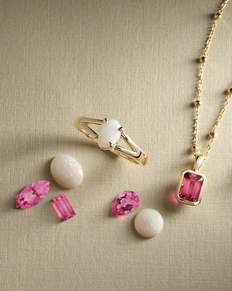 Gold ring with opal, pink gemstones, and a gold necklace with a pink pendant.