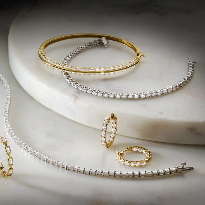 Elegant gold and silver bracelets with sparkling stones displayed on a marble surface.