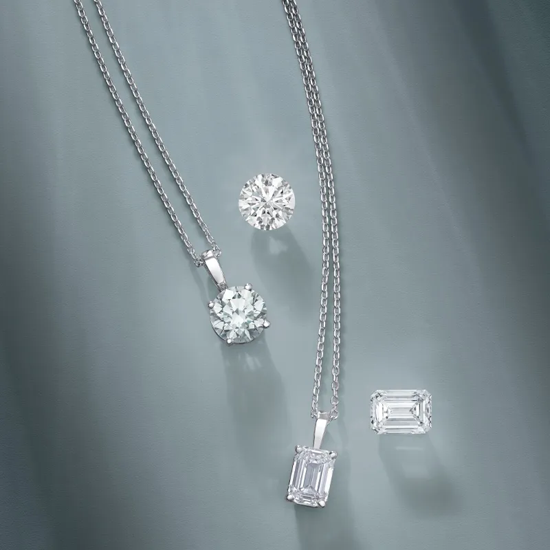 Elegant diamond necklaces featuring round and emerald-cut stones on a soft gray background.