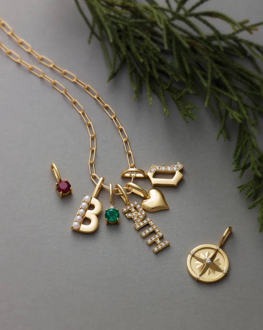 Gold personalized necklace with charms including letters, gemstones, and a compass pendant.