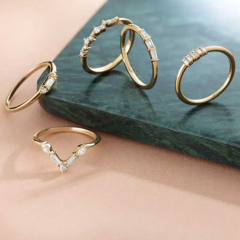 Five elegant gold rings with diamonds displayed on a green stone surface.
