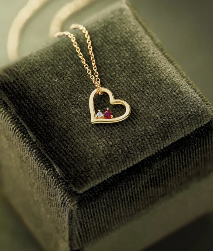 Gold heart necklace with gemstones on a velvet box.