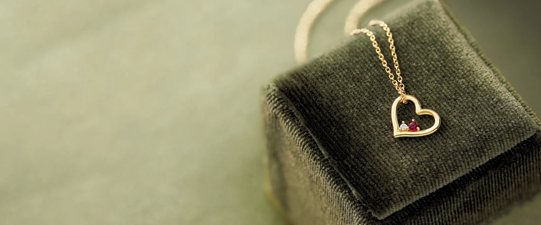 Gold heart necklace with gemstones on a velvet box.
