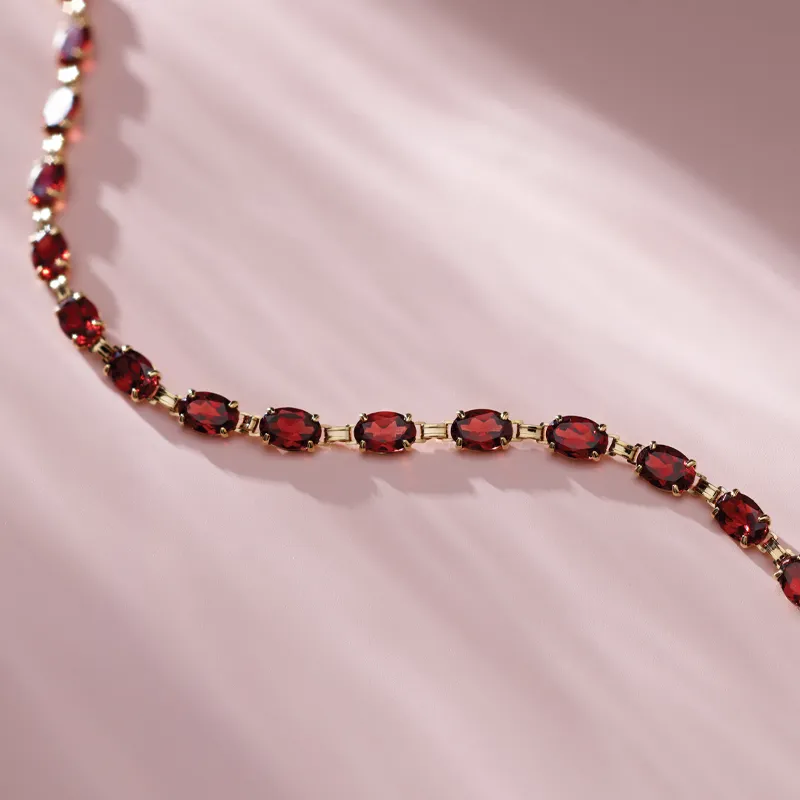 Elegant red gemstone bracelet with gold accents, displayed on a soft pink background.