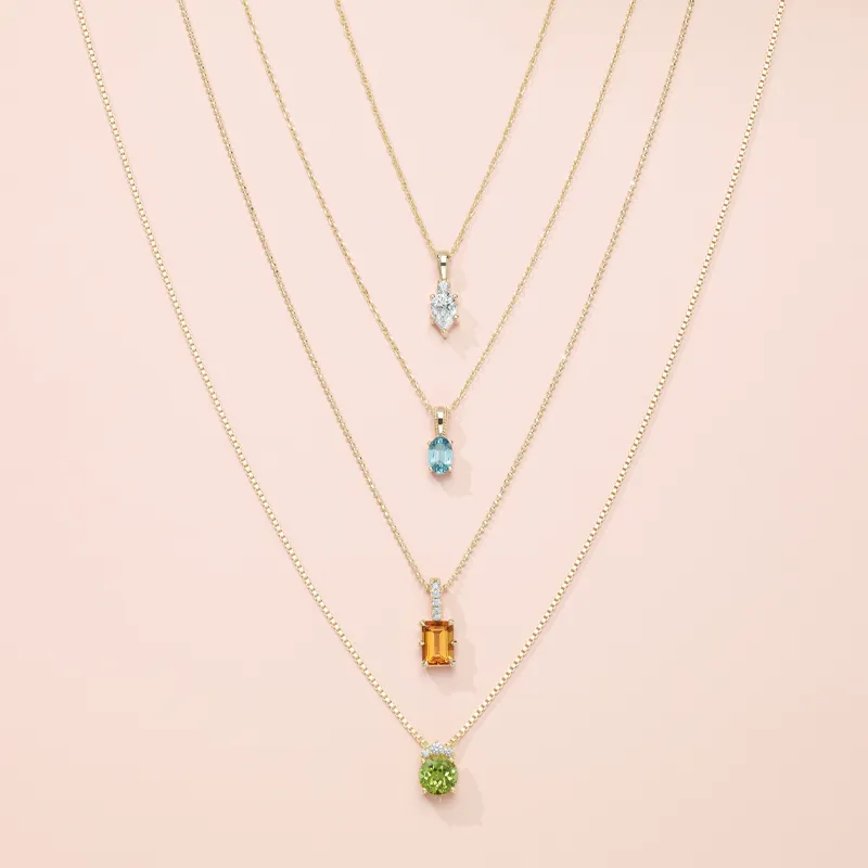Five layered gold necklaces featuring colorful gemstone pendants on a soft pink background.