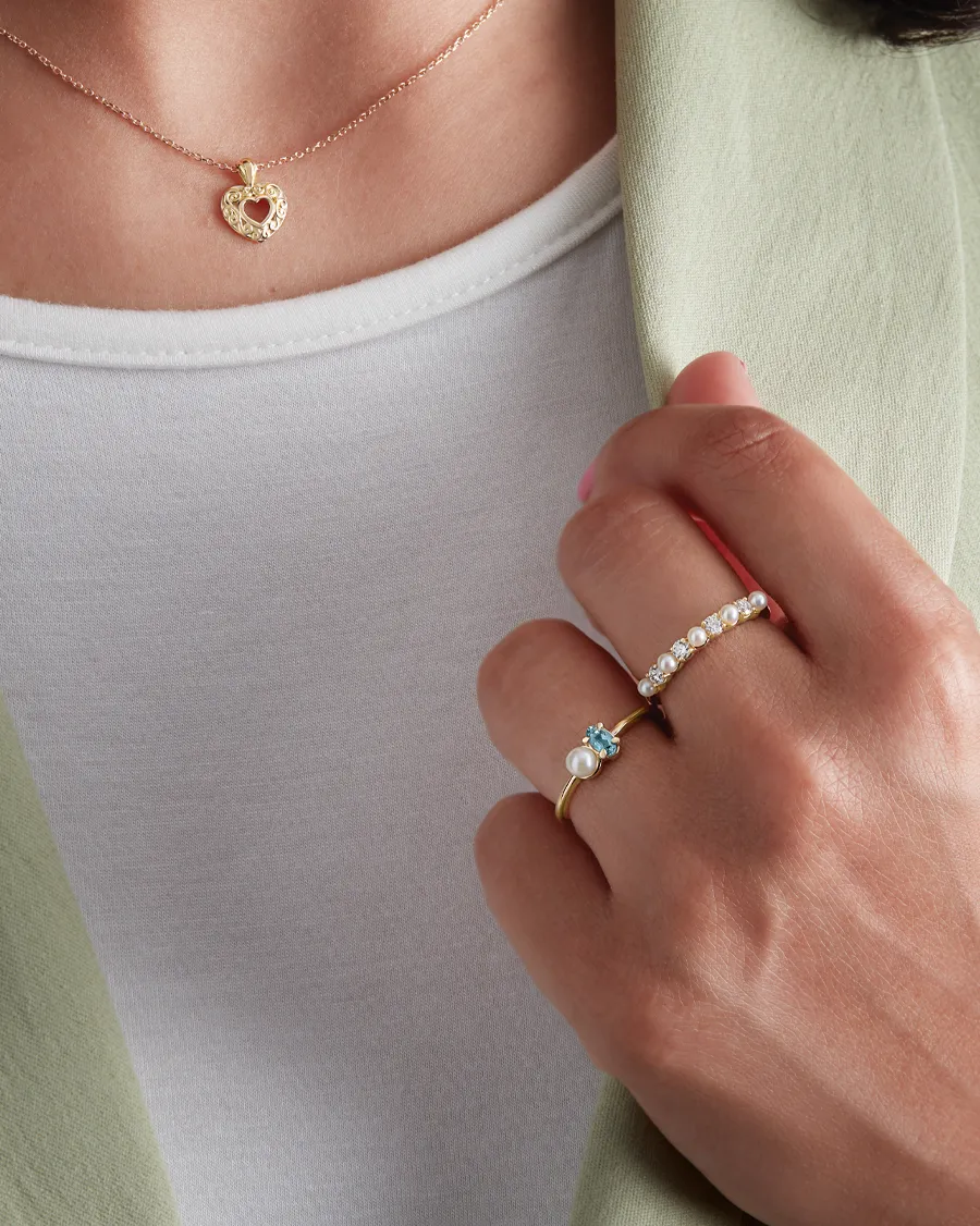 Close-up of a heart necklace and two rings featuring pearls and gemstones. Click to Shop Now at Mathews & Peters.