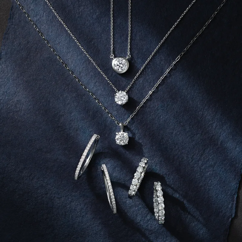 Elegant silver necklaces and diamond rings displayed on a dark surface, showcasing fine jewelry.