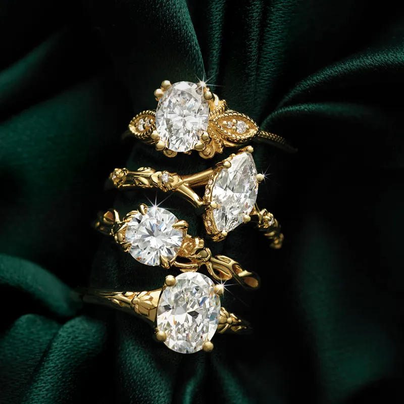 Four elegant gold engagement rings with sparkling diamonds on a dark green fabric background.
