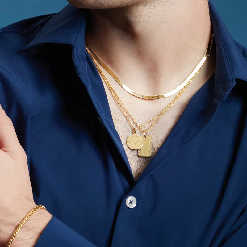 Close-up of a man wearing layered gold necklaces over a blue shirt, showcasing men's jewelry.