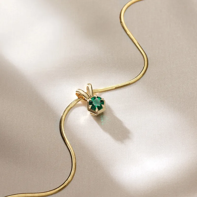 Elegant gold necklace featuring a green gemstone pendant, displayed on a soft fabric background.
