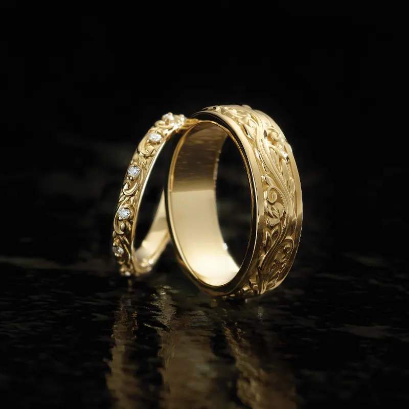 Two intricately designed gold wedding bands, one with diamonds, reflecting light against a dark background.