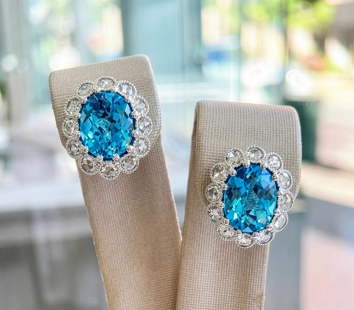 Elegant blue gemstone earrings with diamond accents on display stand.
