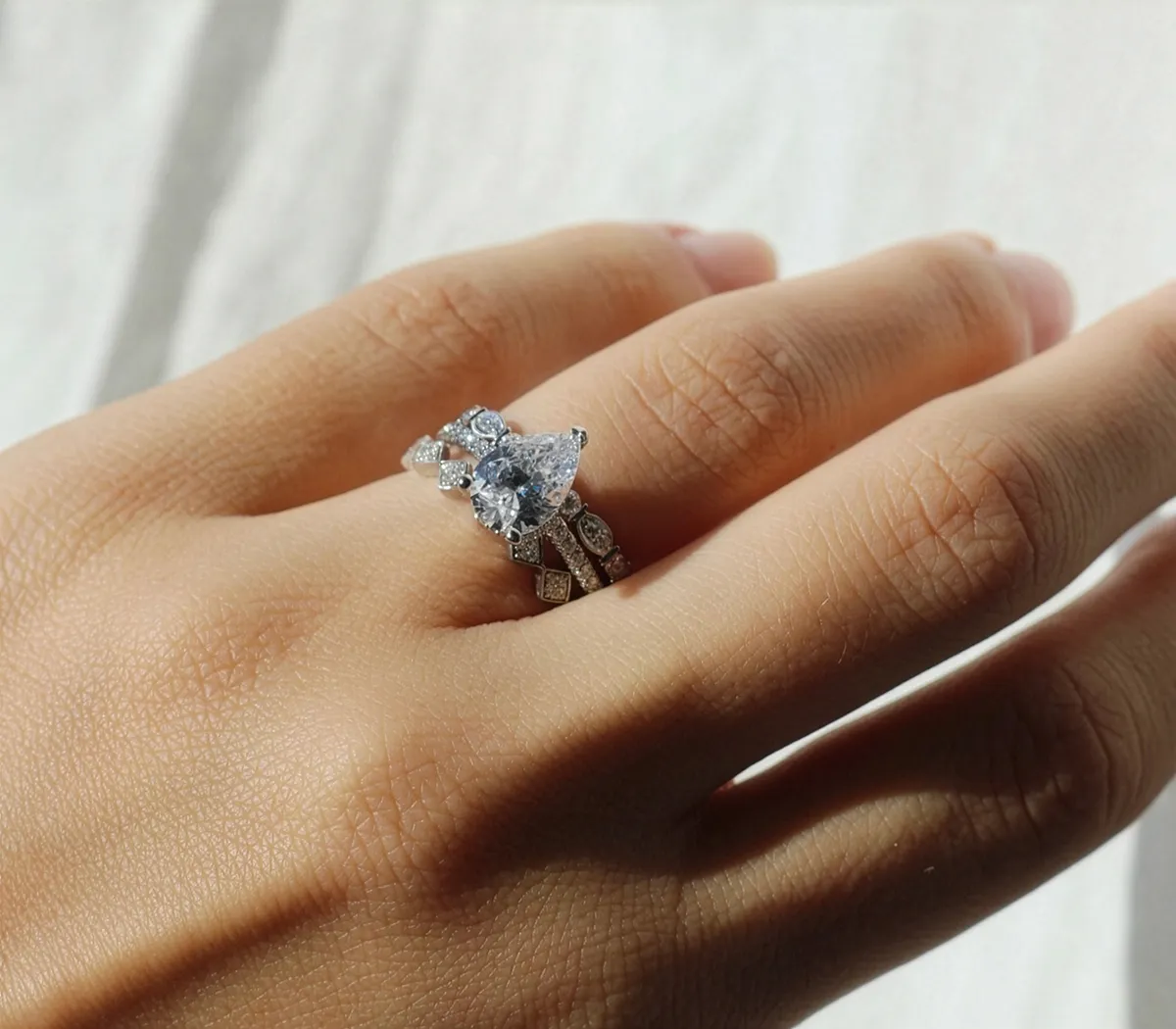A hand wearing a pear-shaped diamond ring with intricate band design.