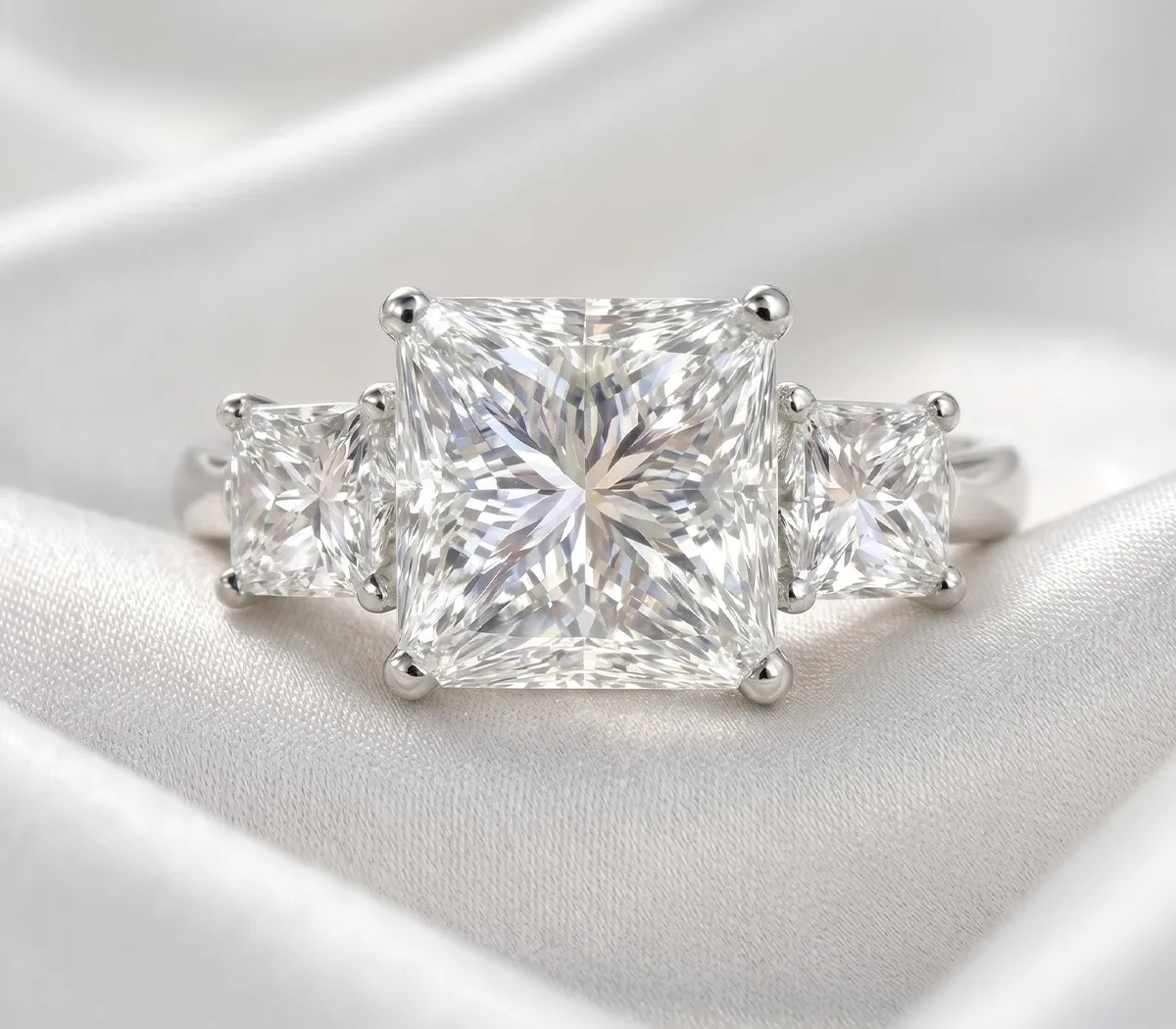 Three-stone diamond ring with a large center stone on a silky white fabric background.