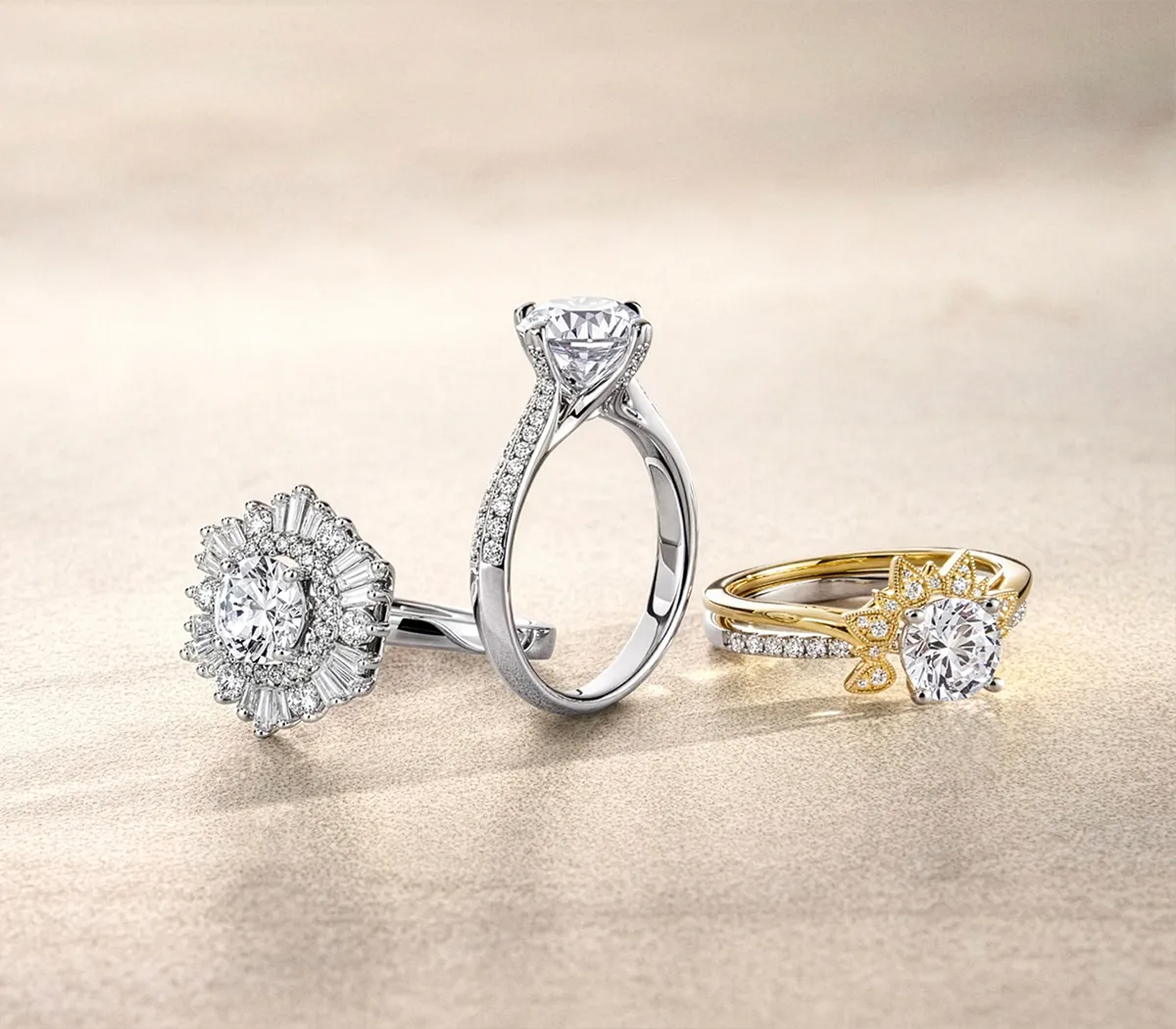 Three elegant diamond rings with intricate designs on a beige background.