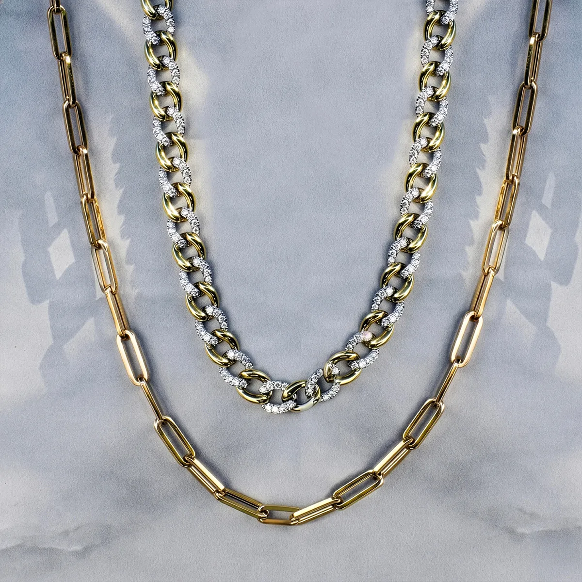 Two gold and diamond chain necklaces displayed on a gray background.