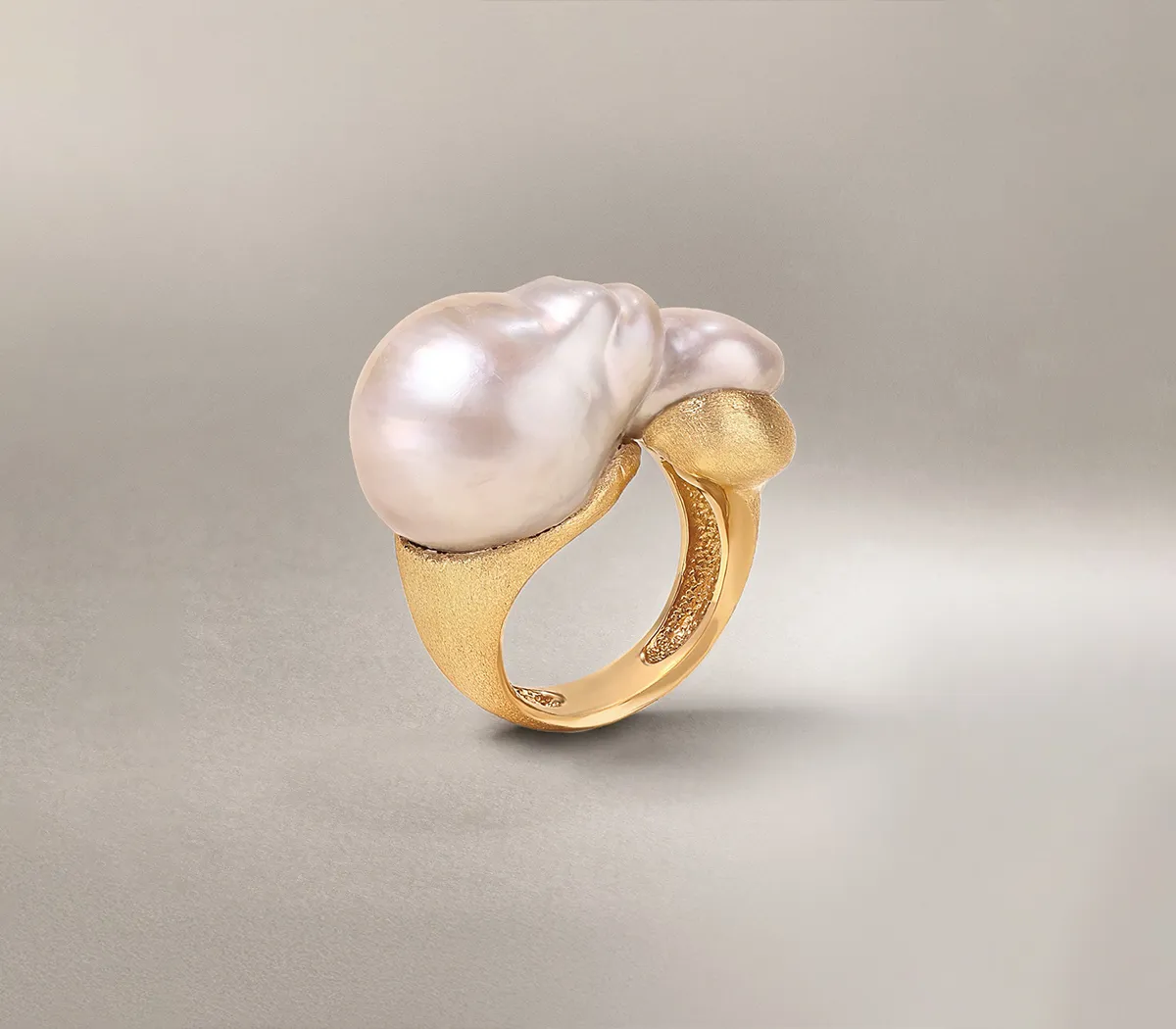 Gold ring with a large, irregular pearl on a neutral background.