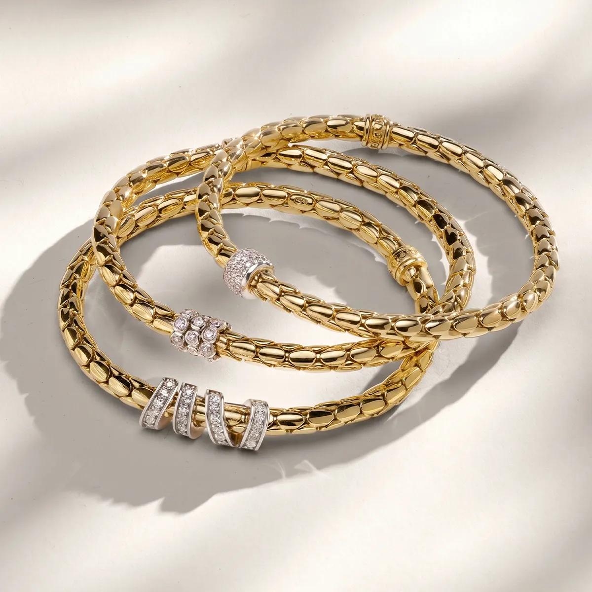 Three gold bracelets with diamond accents on a light background.