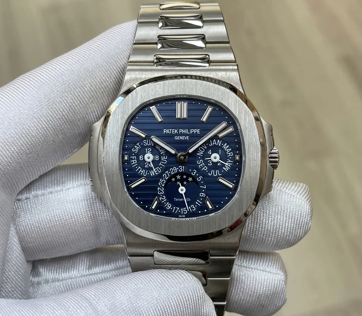 Luxury silver watch with blue dial and multiple subdials held by a gloved hand.