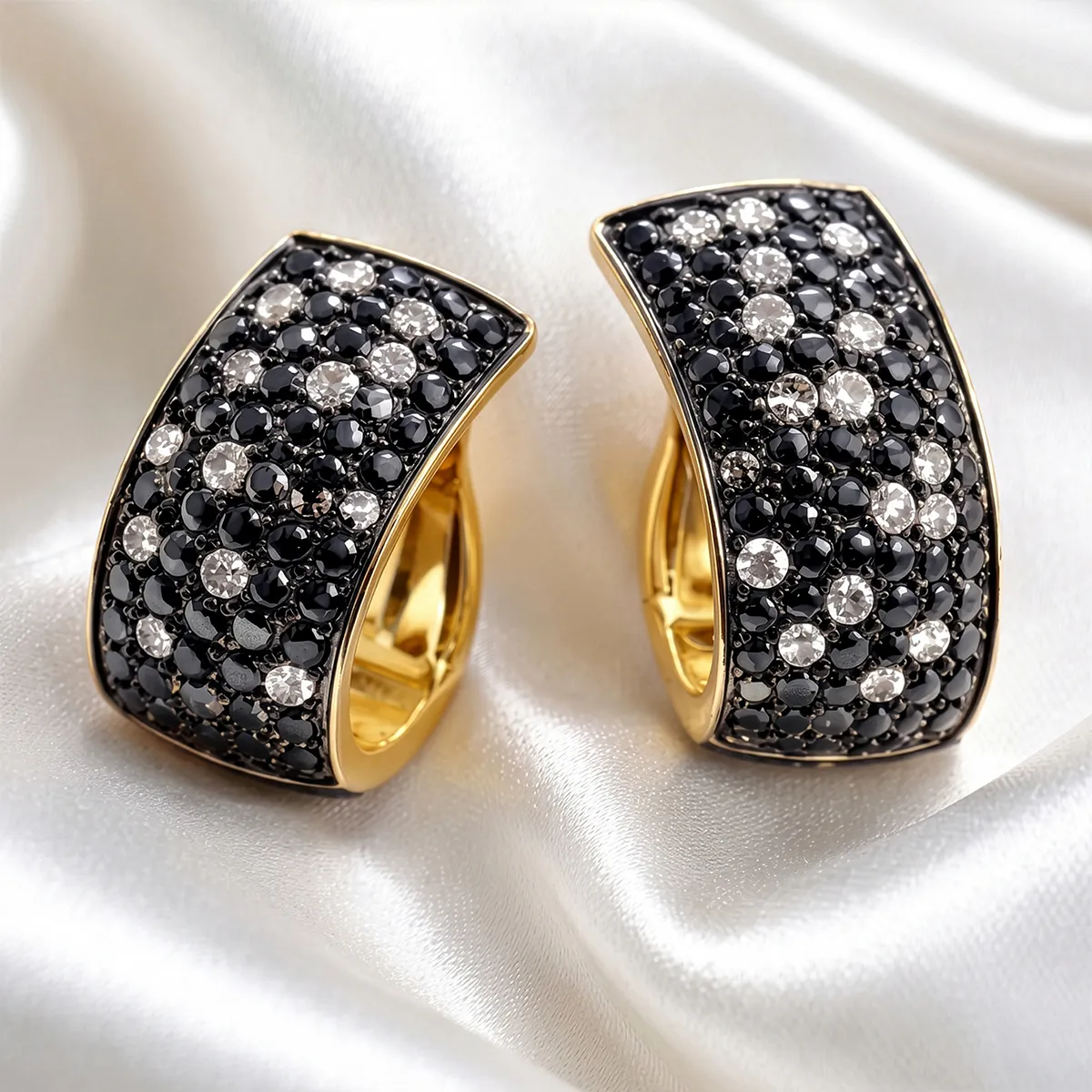 Gold earrings with black and white diamonds on a silky white fabric background.