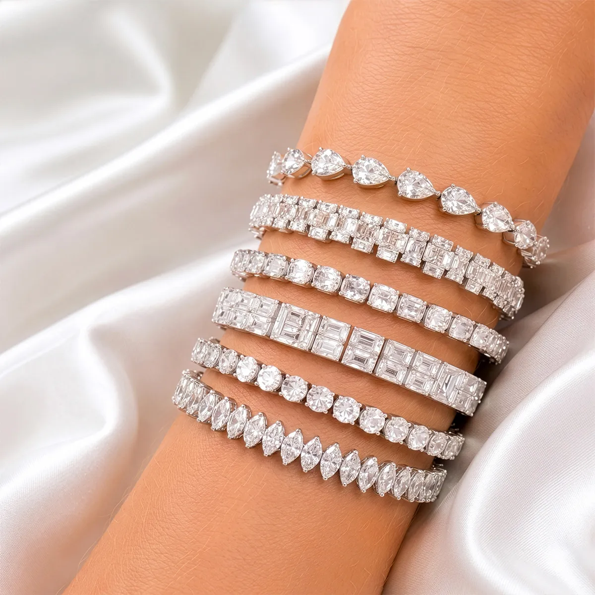 Elegant diamond bracelets on wrist over silky fabric background.