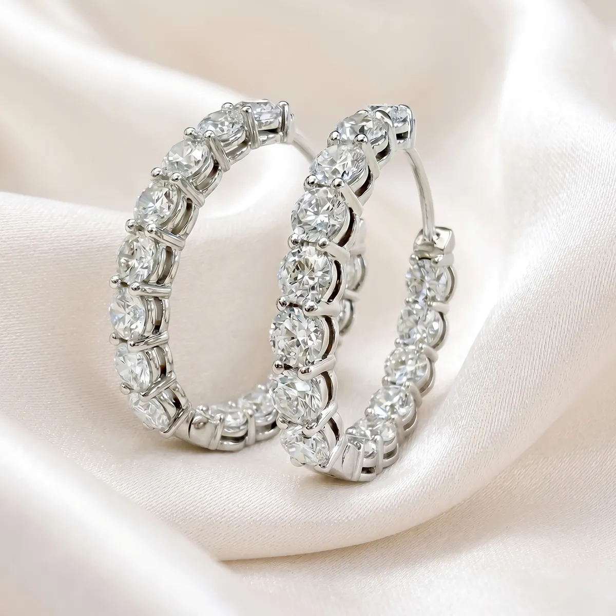 Diamond hoop earrings with round stones on a silky white background.