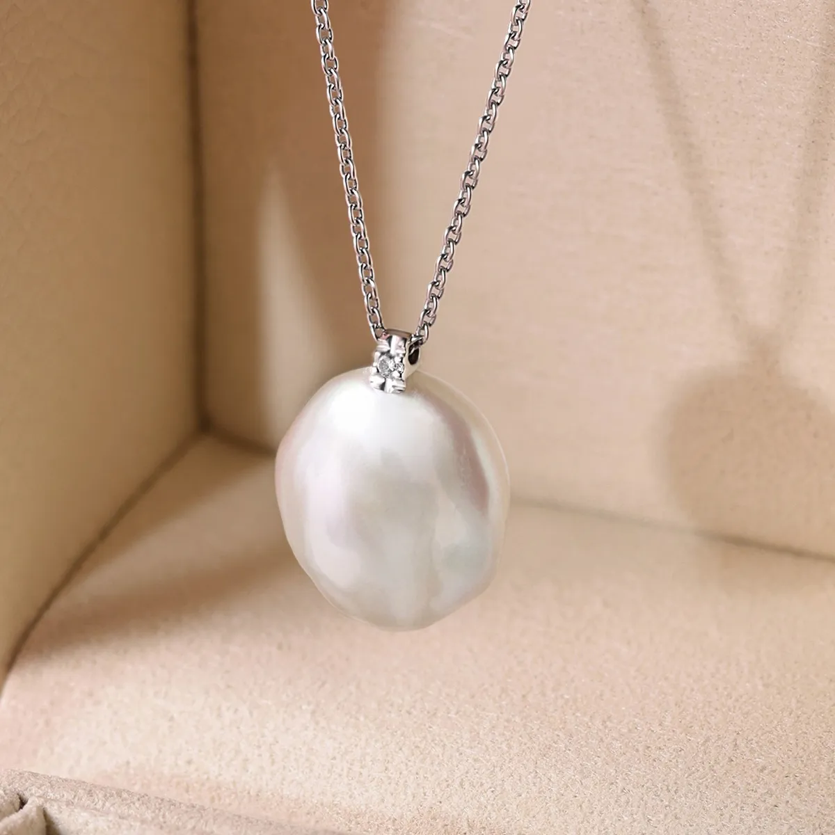 Elegant pearl pendant necklace on a silver chain displayed in a jewelry box.