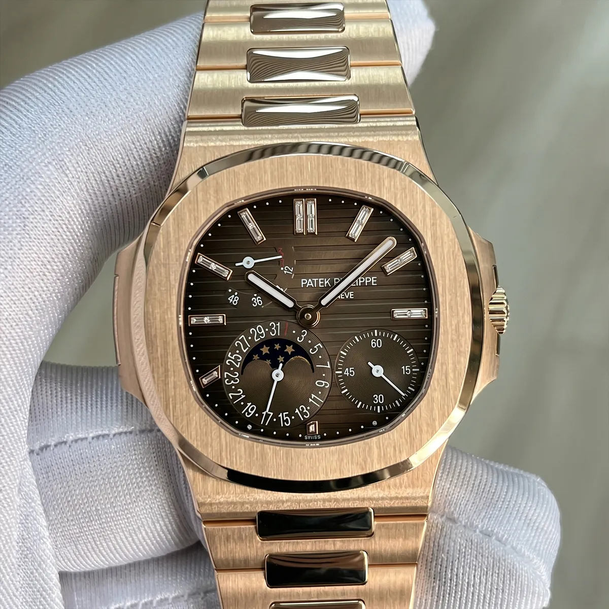 Luxury gold watch with moon phase and date display on a gloved hand.