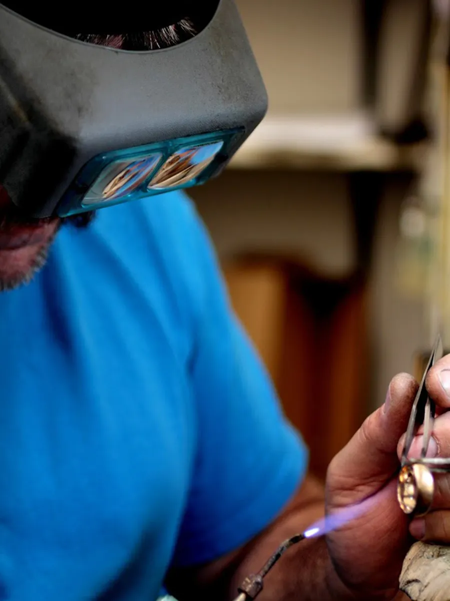 A jeweler wearing magnifying glasses works on a piece with a torch.