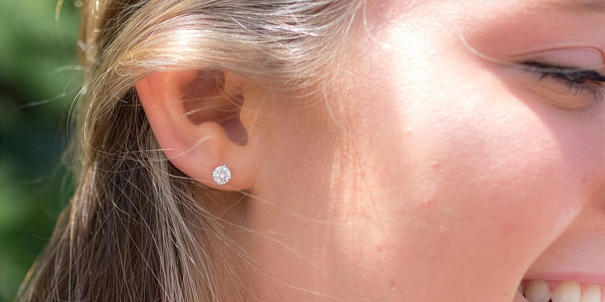 Close-up of a woman's ear wearing a diamond stud earring, with a smiling profile.